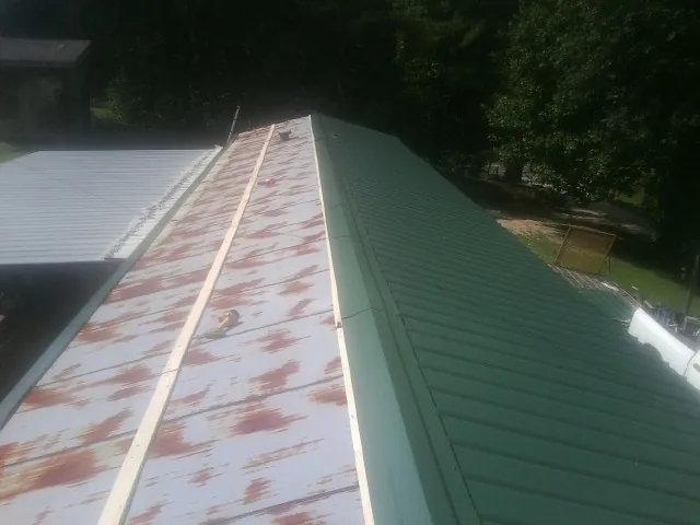 Old rusted panels beside newly installed green metal roofing — Wind Damage Roof Repair by Roofing Brothers in Duluth