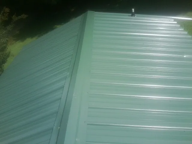 New green metal panels meeting at the ridge of a roof — Flat Roof Repair work by our crew in Duluth