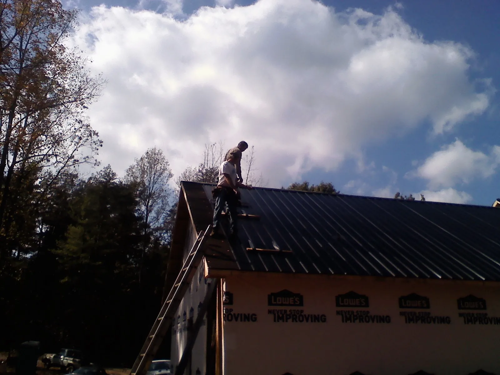Roofer fastening dark metal panels high against a cloudy sky, from a Roof Inspection job in Duluth