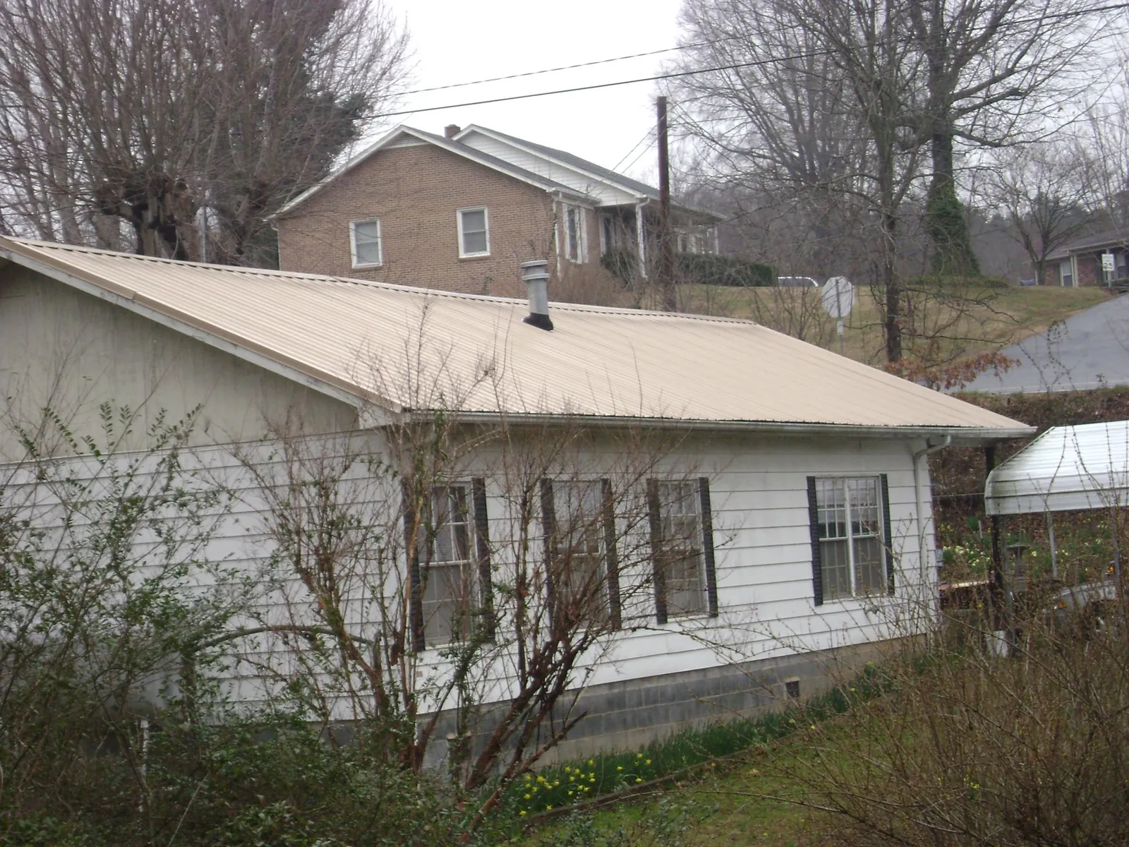 Tan metal roof on a white sided house set into a hillside — Commercial Roofing by Roofing Brothers in Duluth